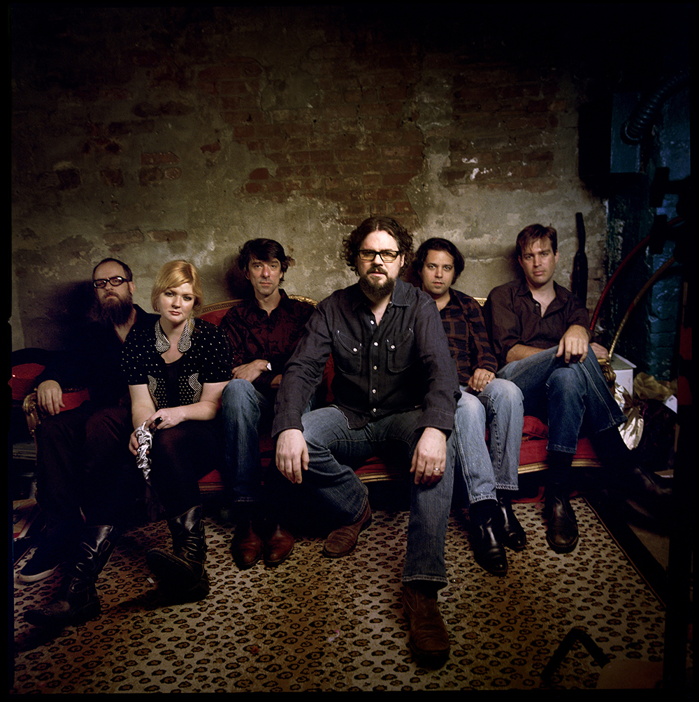 The Drive-By Truckers sitting in a dark room, stuffed onto a couch